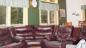 A spacious living room with a large leather sectional sofa, a wooden coffee table, and a ceiling fan. - Large Cabin with WiFi. Great Location: near Castle Rock + WI Dells (Friendship)