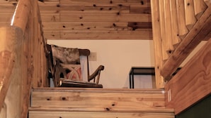 A wooden staircase with a handrail, leading to a room with a chair and a small table. - Large Cabin with WiFi. Great Location: near Castle Rock + WI Dells (Friendship)