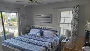 Ein Schlafzimmer mit einem Bett, einem Nachttisch, einer Lampe, einem Deckenventilator und Blick ins Freie.