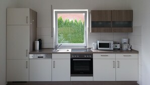 A modern kitchen with white cabinets, a built-in oven, a microwave, and a window with a view of trees.