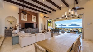 A spacious living area with a large wooden dining table, white sofas, and a TV mounted on the wall. - Gorgeous Views, 2 Masters, 3 more En Suites (Cabo San Lucas)