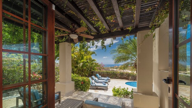 A covered patio with wooden furniture, a ceiling fan, and a view of a swimming pool and tropical vegetation. - Gorgeous Views, 2 Masters, 3 more En Suites (Cabo San Lucas)