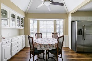 A kitchen with a dining area, a ceiling fan, a refrigerator, and a bay window with blinds.