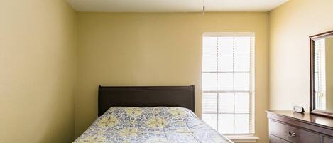 A bedroom with a bed, a ceiling fan, a window with blinds, and a dresser.