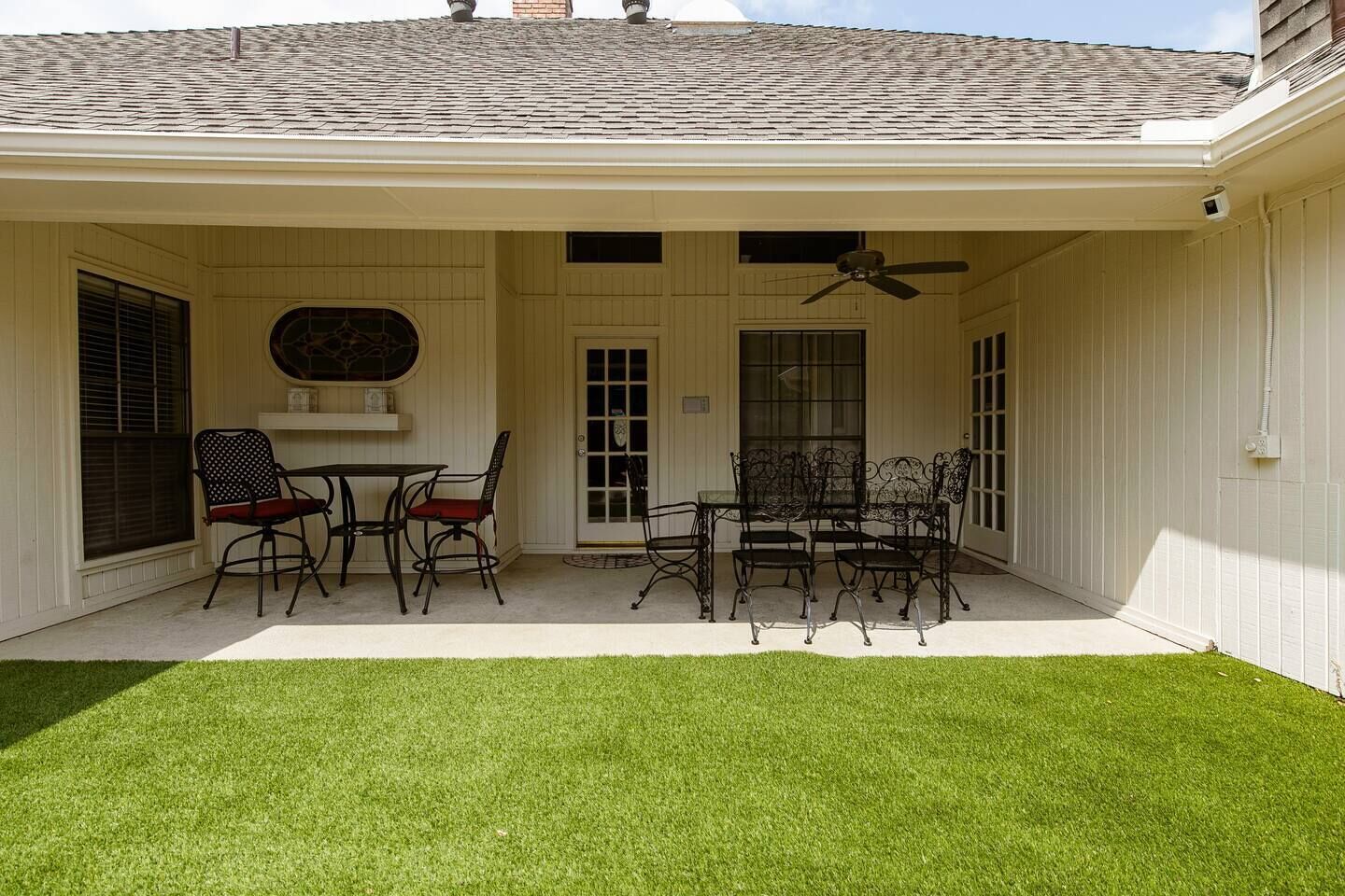 Une terrasse couverte avec une table et des chaises, un ventilateur de plafond et un petit coin jardin.