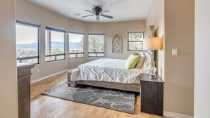 A bedroom with a bed, a ceiling fan, large windows, a rug, and a nightstand. - "The View in Prescott," a Custom Home With 3 Patios + Fire Pit, Near Downtown (Prescott)