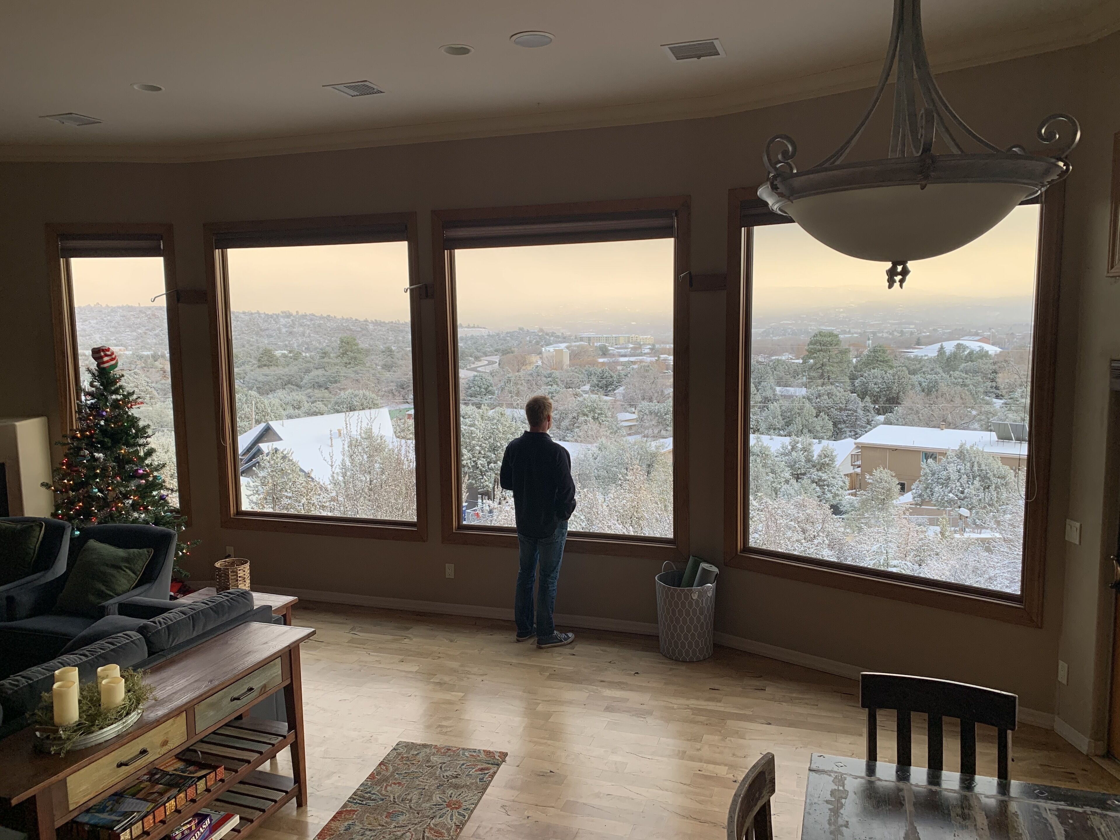 A room with large windows, a Christmas tree, a dining table, and a sofa.