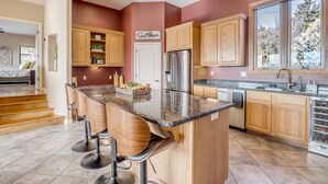 A modern kitchen with wooden cabinets, a stainless steel refrigerator, and a large island with bar stools. - "The View in Prescott," a Custom Home With 3 Patios + Fire Pit, Near Downtown (Prescott)