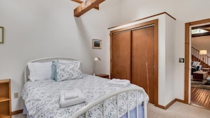 A bedroom with a bed, a wooden wardrobe, a small bedside table, and a window with a wooden beam. - Brewster Retreat Near Bay Beaches & Dining (Brewster)
