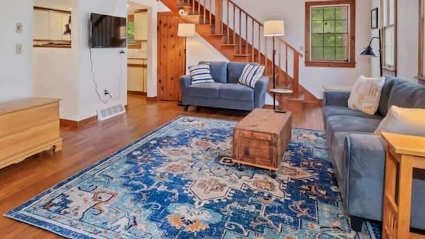 A spacious living room with a wooden ceiling, a staircase, a blue patterned rug, and a grey sofa. - Brewster Retreat Near Bay Beaches & Dining (Brewster)