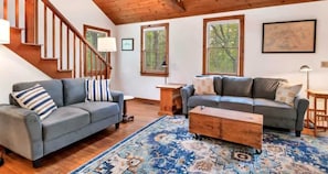A living room with two sofas, a wooden coffee table, a rug, a staircase, and large windows.