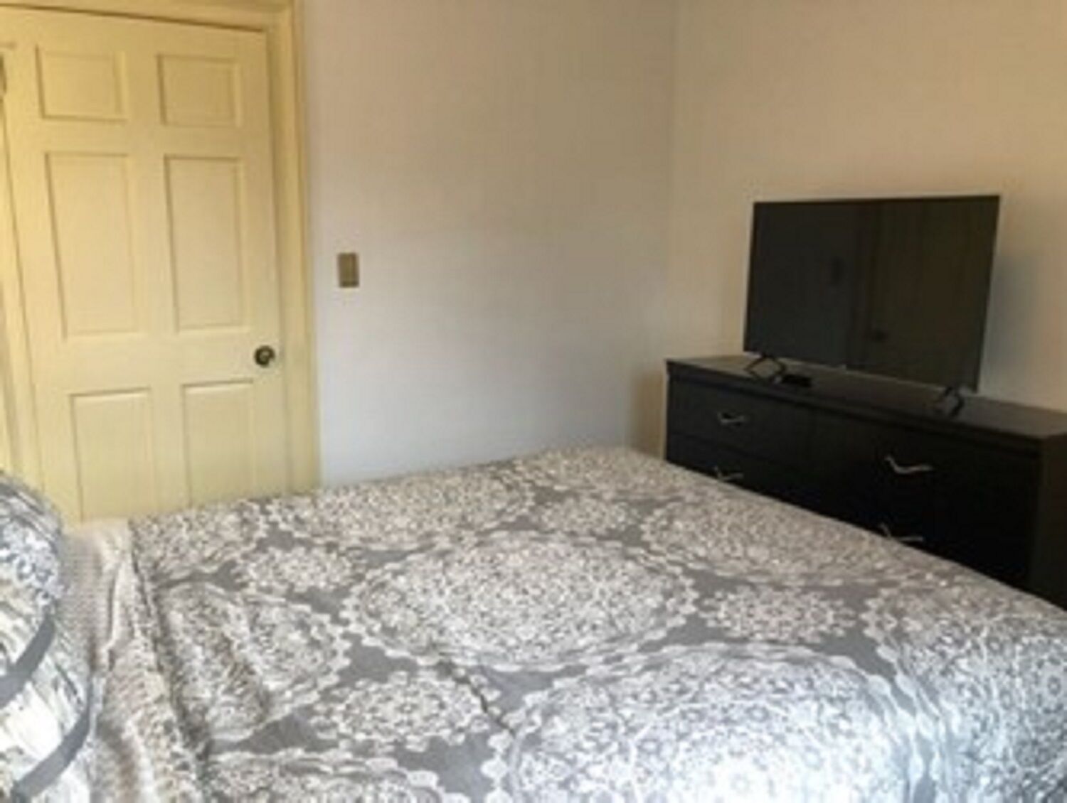 A bedroom with a bed, a dresser, a television on top of the dresser, and a door.