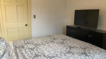 A bedroom with a bed, a dresser, a television on top of the dresser, and a door.