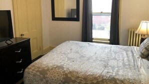 A bedroom with a bed, a dresser, a mirror, and a window with curtains.