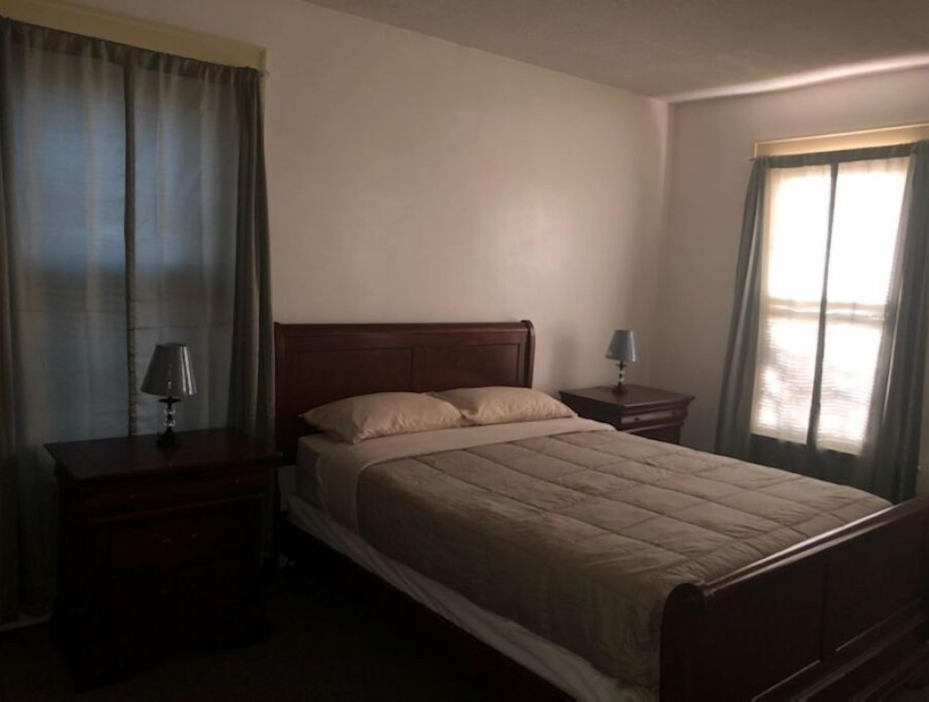 Een standaard hotelkamer met een eenpersoonsbed, twee nachtkastjes en een raam met gordijnen.