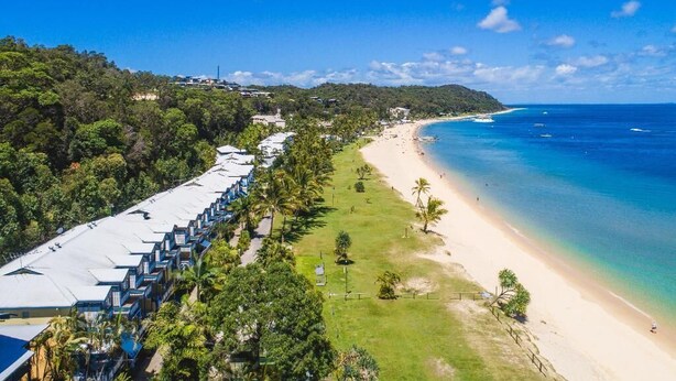 A coastal hotel with a long row of rooms overlooking a beach and the ocean.
