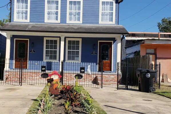 A two-story house with a blue exterior, a front porch, and a small garden with a welcome sign.