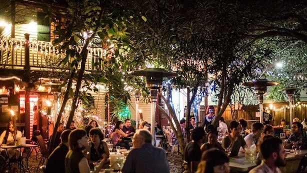 An outdoor dining area with tables and chairs, surrounded by trees and illuminated by string lights. - 11NOLA Living In The Heart Of Many Attractions  (New Orleans)