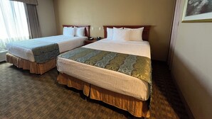 Habitació d'hotel amb dos llits, un gran finestral amb cortines, un quadre a la paret i un termòstat penjat a la paret.