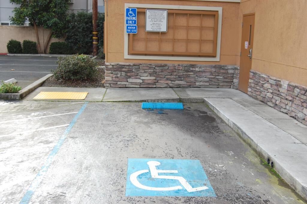 Un área de estacionamiento con un espacio reservado para discapacitados, un hidrante y la entrada a un edificio.