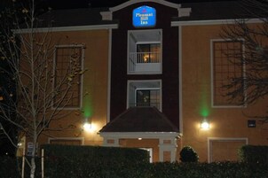 Un edificio con un letrero que dice "Pleasant Hill Inn". Presenta una fachada simétrica con dos ventanas a cada lado, una entrada central y un pequeño balcón.