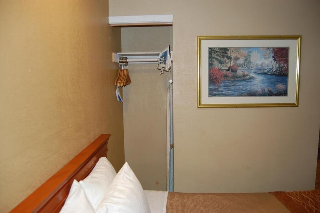 A hotel room with a bed, a painting of a landscape, and a window with a curtain rod.