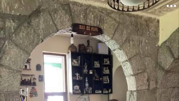 A stone-walled bar area with a wooden bench, a wine rack, and a sign reading "BAR DE PAPA".