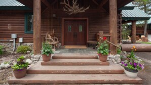 A wooden cabin with a porch, steps leading to a door, and potted plants.