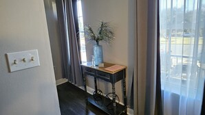 A room with a dark wooden floor, a small table with a vase, and a window with curtains. - NOLA Living In The Heart Of Many Attractions (New Orleans)