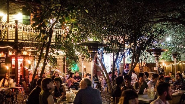 An outdoor dining area with tables and chairs, surrounded by trees and illuminated by string lights. - NOLA Living In The Heart Of Many Attractions (New Orleans)