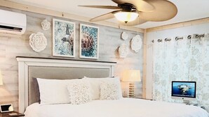 Un dormitorio moderno con una cama grande, un ventilador de techo y un televisor en la pared.