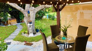 Un patio al aire libre con un porche de madera, una mesa con sillas y el tronco decorativo de un árbol.