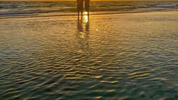 Dos personas de pie en la playa al atardecer.