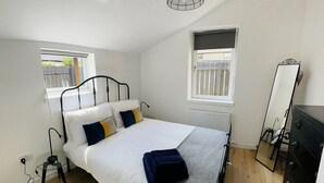 Een slaapkamer met een bed, nachtkastje, kaptafel, spiegel en een raam met uitzicht.