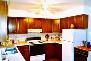 A kitchen with wooden cabinets, a stove, a sink, a refrigerator, and a ceiling fan.
