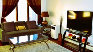 Un salon avec un canapé, une table basse en verre, un téléviseur posé sur un meuble, une lampe et un radiateur.