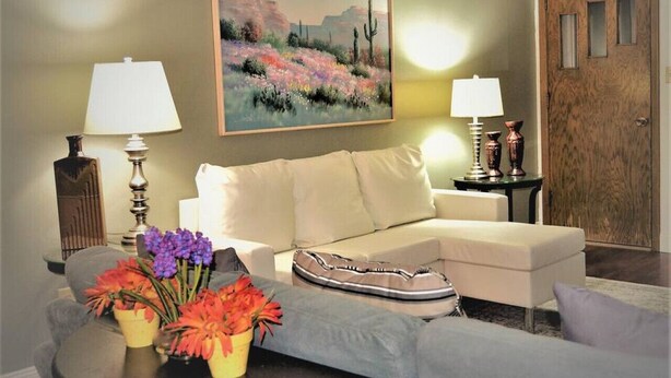 Un salon avec un canapé beige, une table basse ronde ornée de fleurs, deux lampes et un tableau accroché au mur.