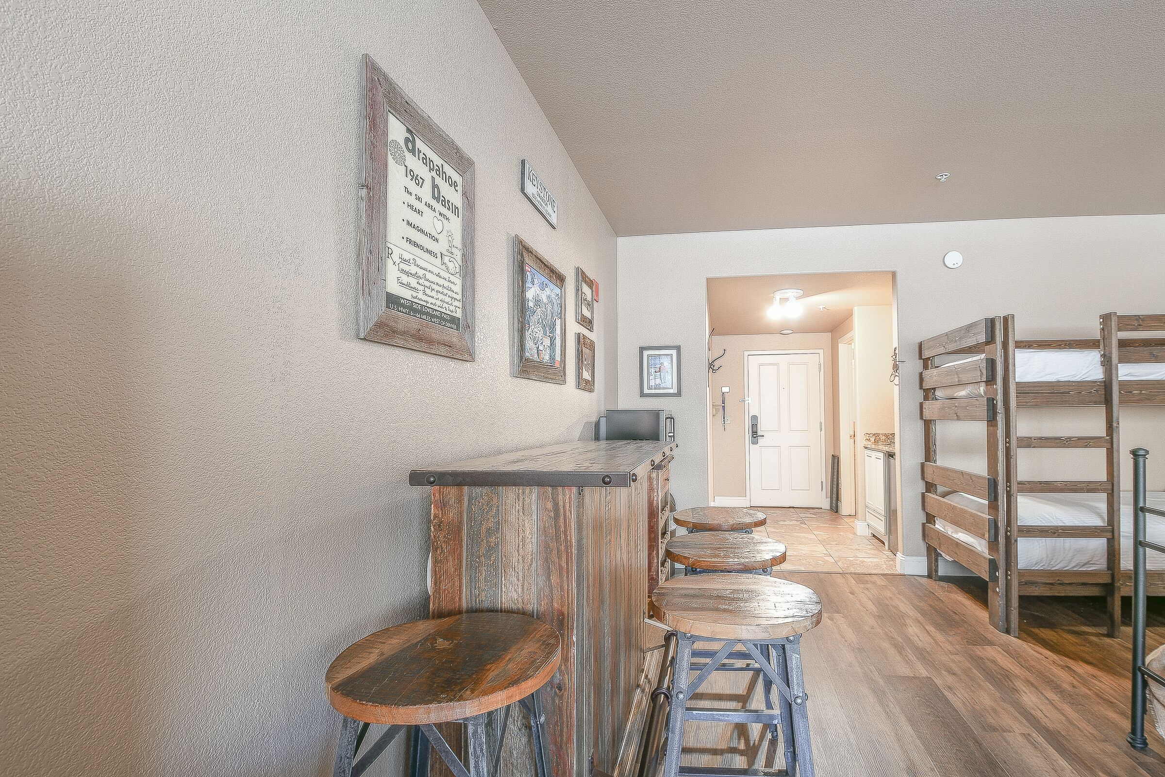 A rustic interior with a bar area, wooden stools, and a loft bed.