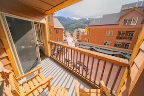 A balcony with wooden chairs and a view of a town with buildings and mountains in the background. - Buffalo Lodge 8352 (Keystone)