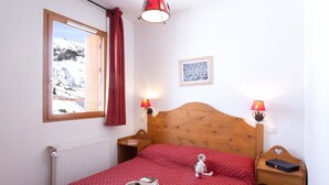 Una camera da letto con una testiera in legno, una finestra che si affaccia su un paesaggio innevato, due abat-jour e un quadro appeso al muro.