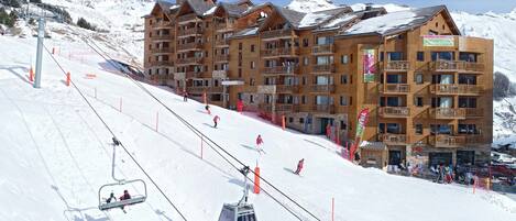 A multi-story wooden building with balconies, ski lifts, and a snowy mountain backdrop.