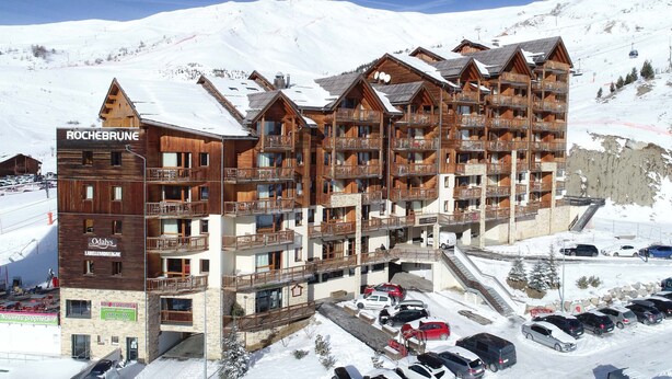 A multi-story wooden hotel with balconies, a ski lift in the background, and a snowy mountain landscape.