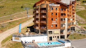 A multi-story wooden building with balconies, a swimming pool, and a ski lift in the background.