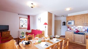 A cozy room with a wooden dining table, chairs, a television, and a kitchen area with wooden cabinets and a microwave.
