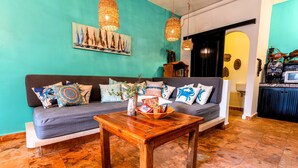Ein gemütliches Wohnzimmer mit grauem Sofa, Couchtisch aus Holz und einer türkisblauen Wand mit einem Segelboot-Gemälde.