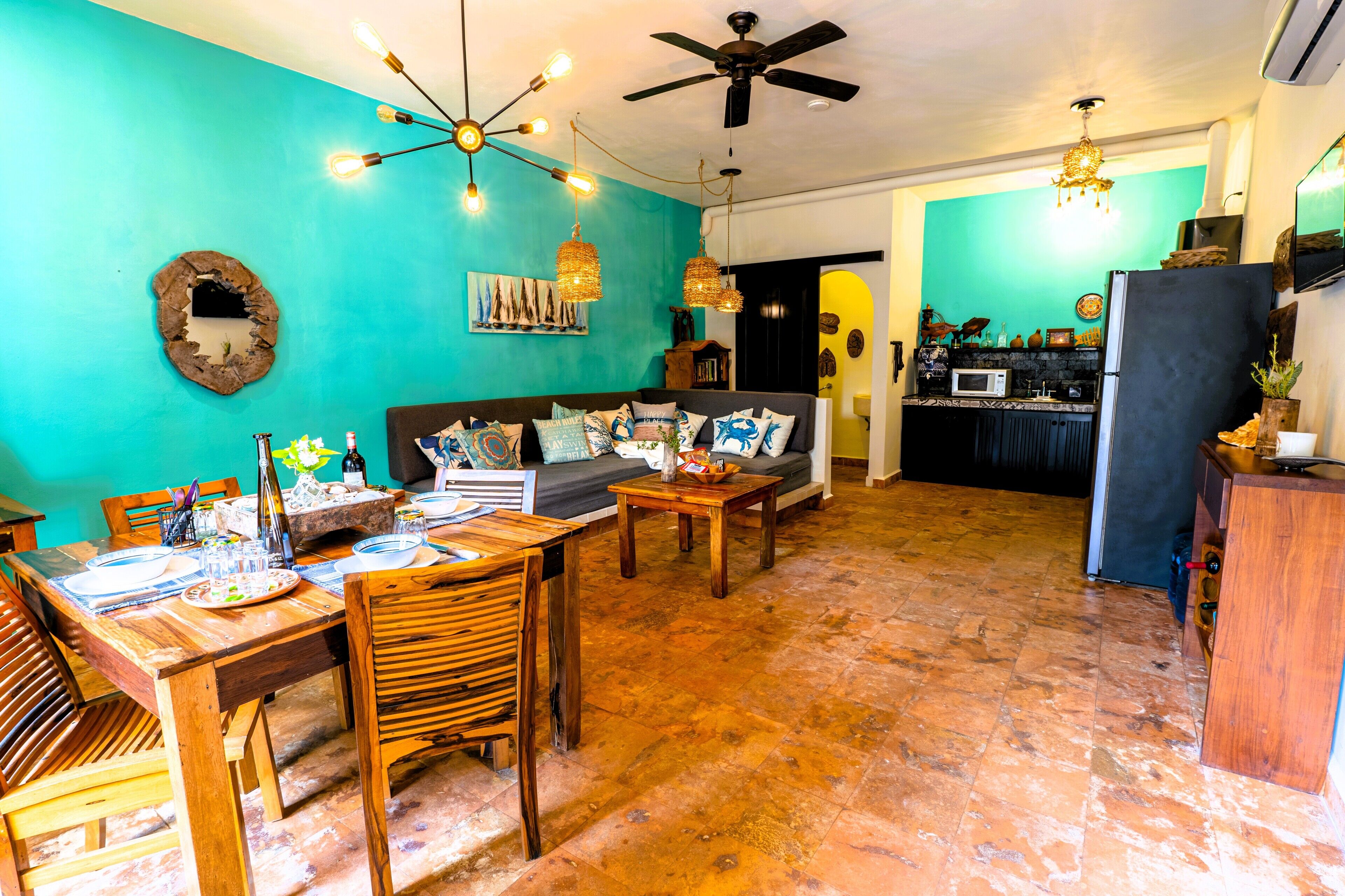A spacious living area with a dining table set for a meal, a sofa with cushions, and a kitchen in the background.