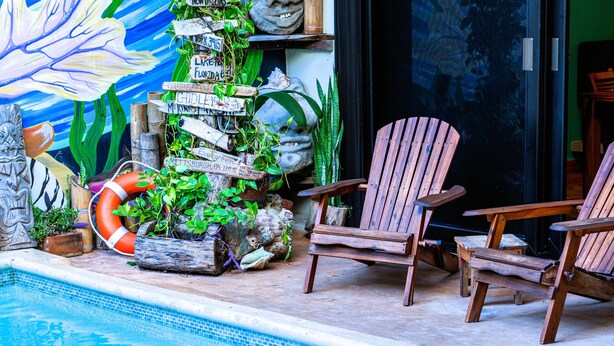 A poolside area with wooden chairs, a lifebuoy, and a wall decorated with signs and plants. - The Jardin Suite lower-level suite, poolside w/kitchen at Boutique Hotel (Isla Mujeres)