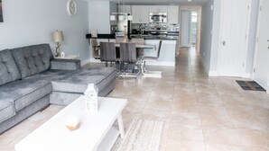 A modern living room with a grey sectional sofa, a white coffee table, and a dining area with a glass table and chairs. A kitchen with stainless steel appliances is visible in the background. - BEAUTIFUL LUXURY APARTMENT CLOSE DISNEY (Kissimmee)