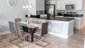 A modern kitchen with a central island, stainless steel appliances, and a dining area with a glass table and chairs. - BEAUTIFUL LUXURY APARTMENT CLOSE DISNEY (Kissimmee)