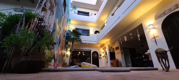 A multi-level building with a central courtyard, featuring a large tree, a mural, and a statue.